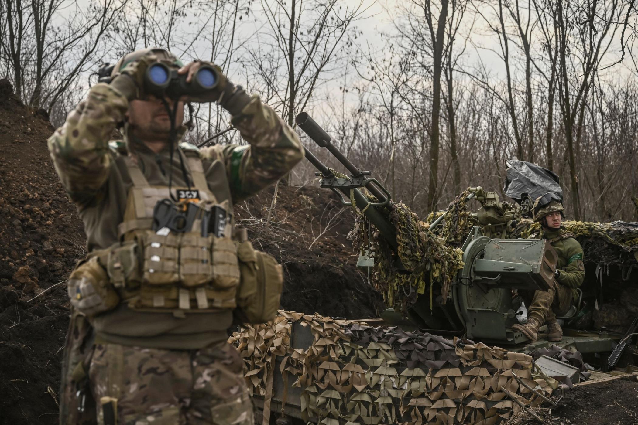 A Ukrainian serviceman (L) looks on with binoculars next to another (R) sitting on an anti-air gun near Bakhmut, Ukraine, March 24, 2023. (AFP Photo)