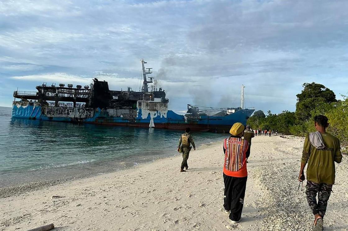 People walking toward the burnt passenger ferry, Basilan province, southern Philippines, March 30, 2023. (AFP Photo)