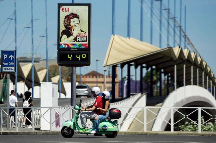 A couple ride a Vespa motorcycle past a street thermometer reading 44 degrees Celsius in Seville, Spain, April 26, 2023. (AFP Photo)